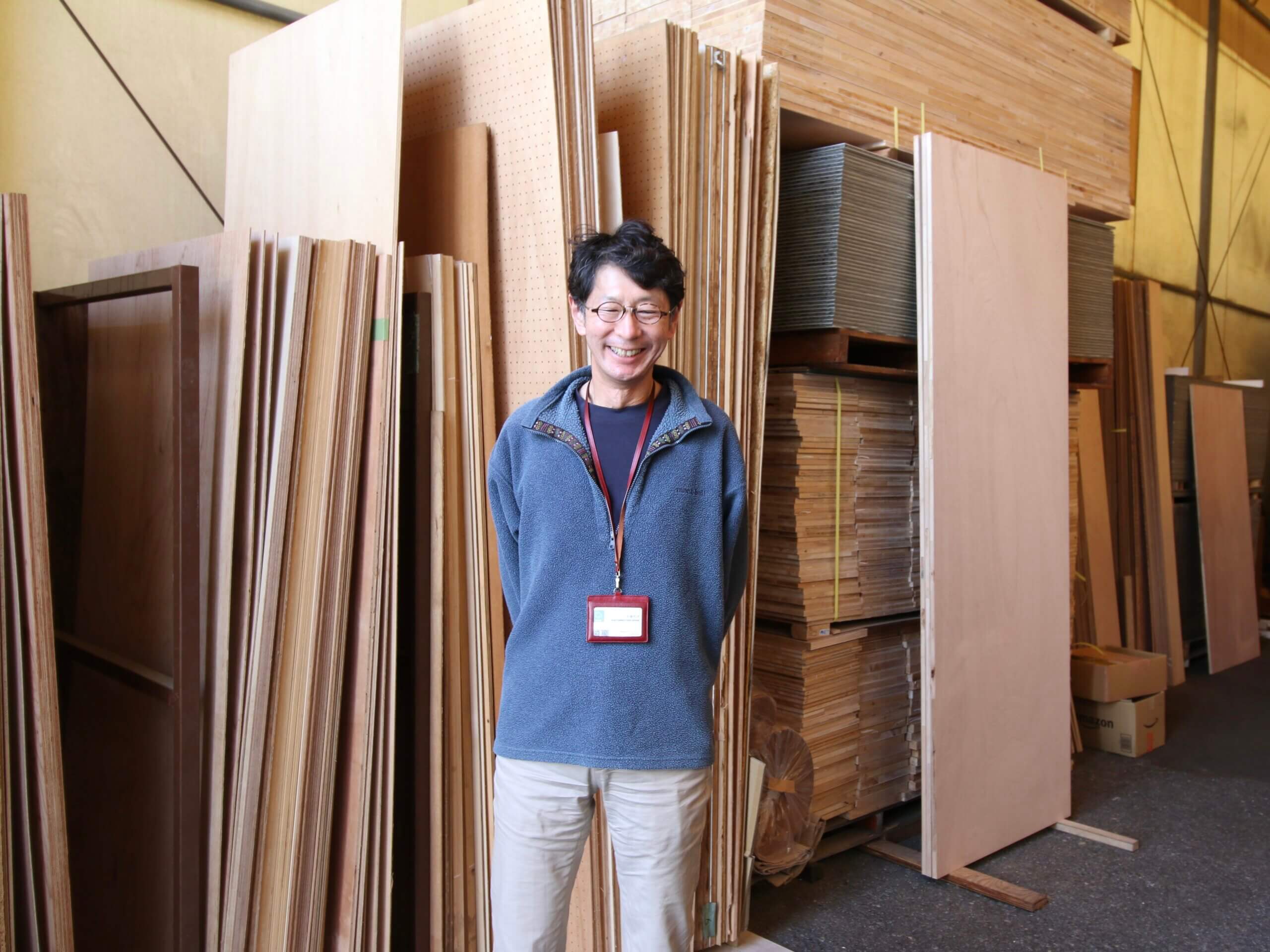 合板が並ぶ前に立つオーナー