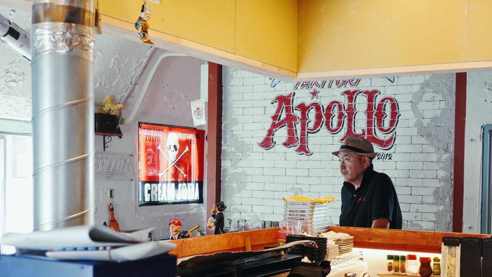 店内のカウンター越しに見える店主とAPOLLOと描かれた壁画