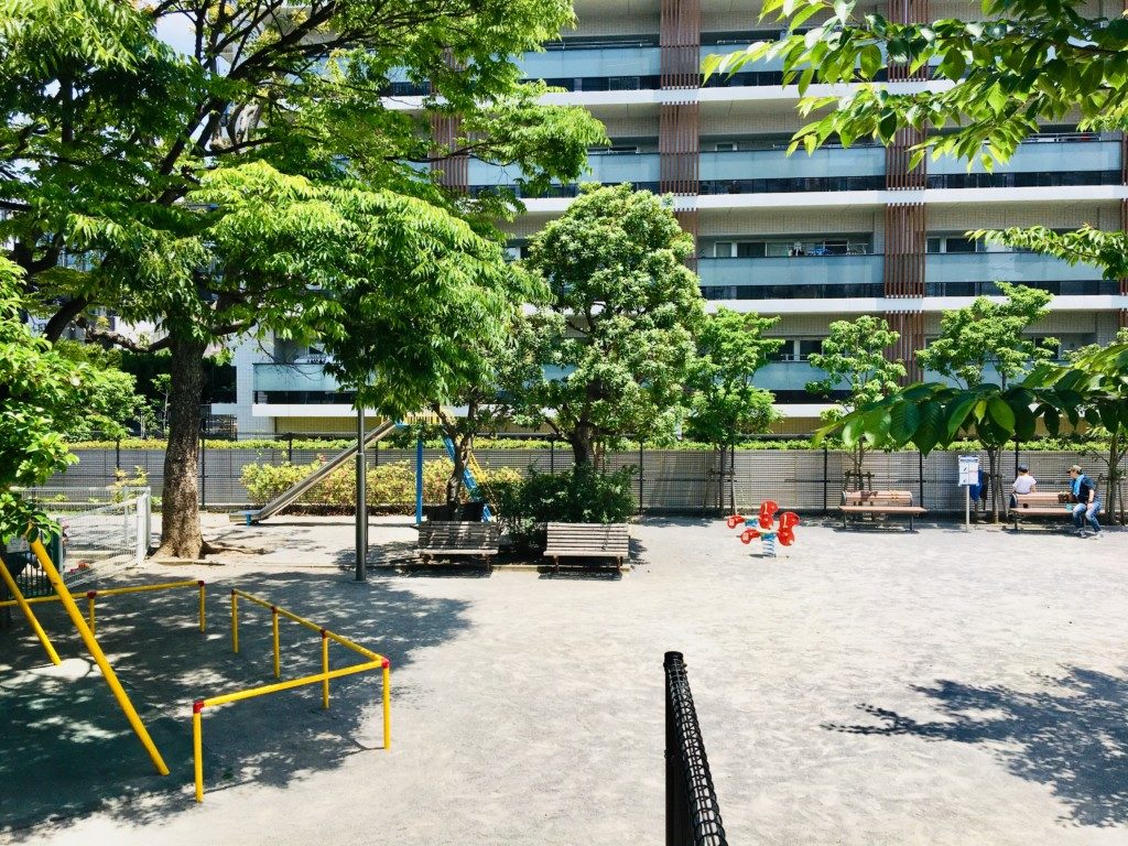 木陰の多い園内の後ろにそびえ建つ大型マンション